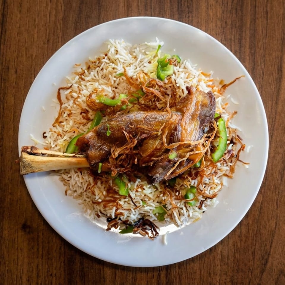 Overhead view of spiced basmati rice topped with a roasted lamb shank, fried onions, and green peppers on a white plate.
