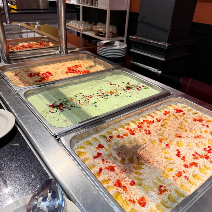 Buffet line with three large trays of middle-eastern dips, including green, white, and orange varieties.