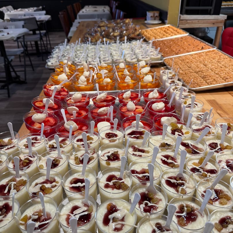 A buffet table laden with rows of Middle Eastern desserts, including puddings, jellies, and pastries.