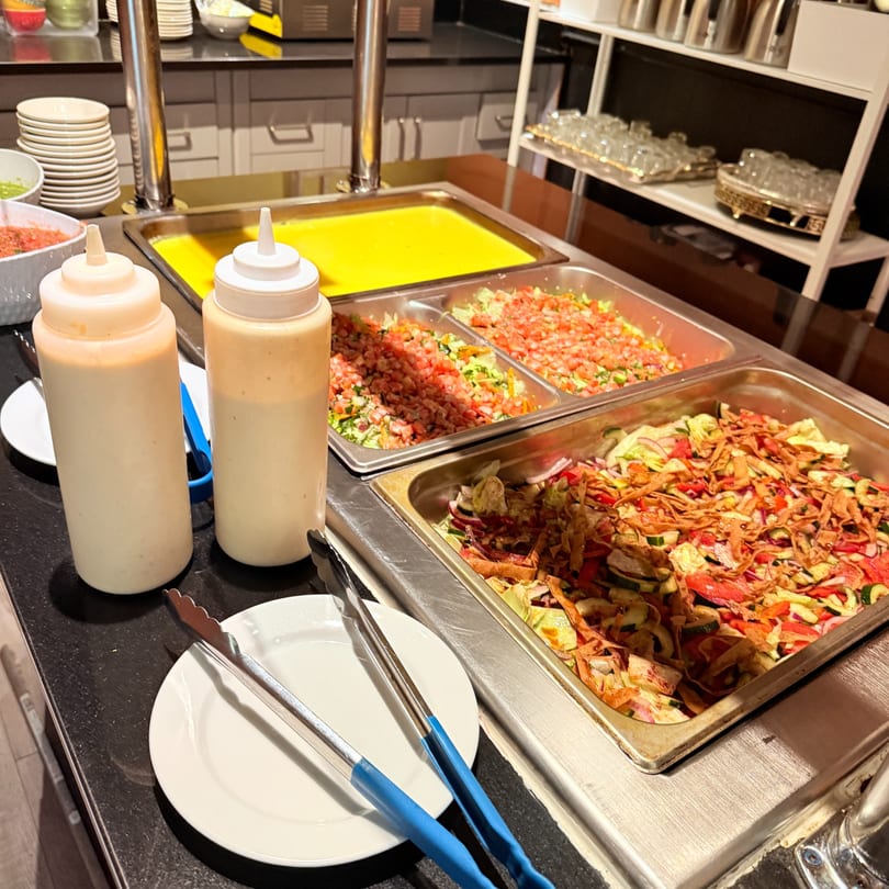 Middle-Eastern buffet with salads, sauces, and a yellow liquid dish, ready for serving.