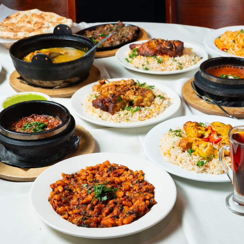 A table laden with various Middle Eastern dishes, including stews, rice, meat, and flatbread.