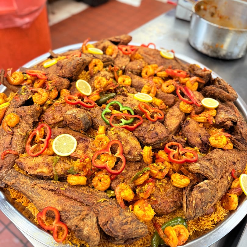A large platter of Middle-Eastern fried fish and shrimp over rice, garnished with bell peppers and lemons.