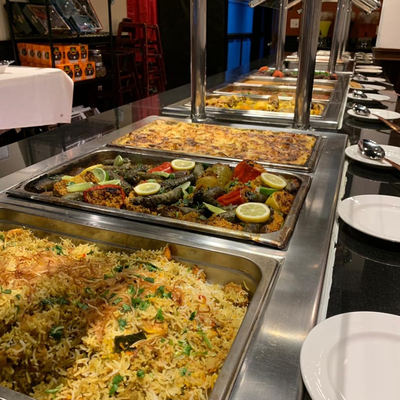 A buffet line at Marib Restaurant with trays of Middle Eastern dishes, including rice and stuffed vegetables.