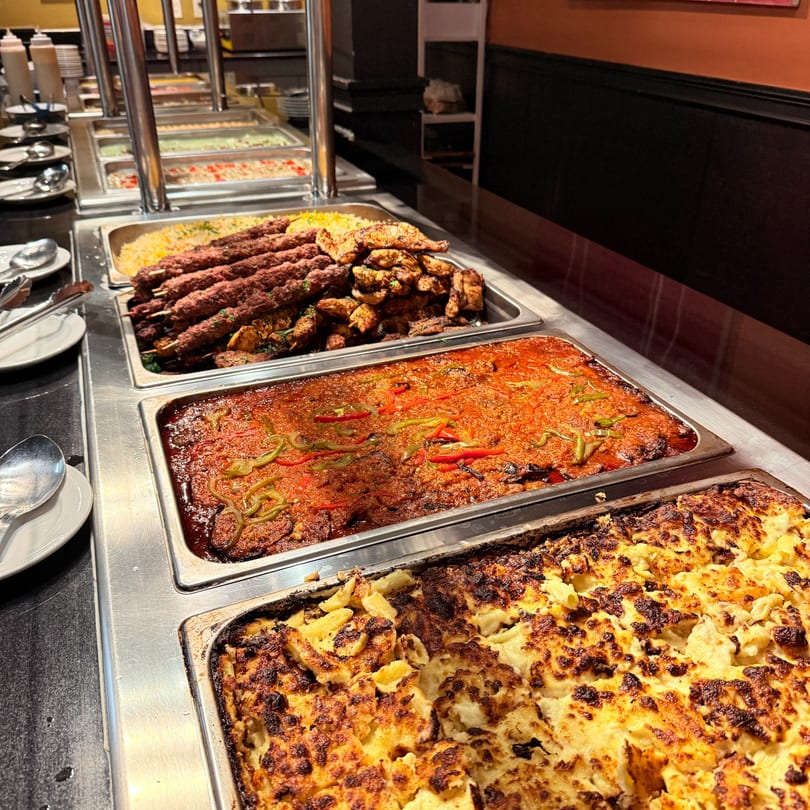 A buffet line at Marib Restaurant with Middle-Eastern dishes like kebabs, stew, and baked pasta.